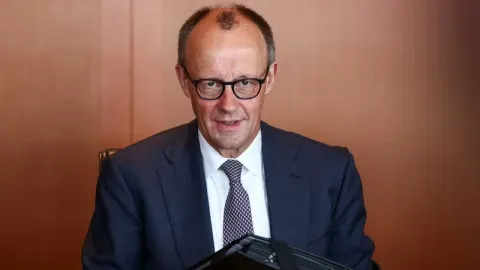 Friedrich Merz nosi naočale i tamno odijelo dok sjedi za stolom.