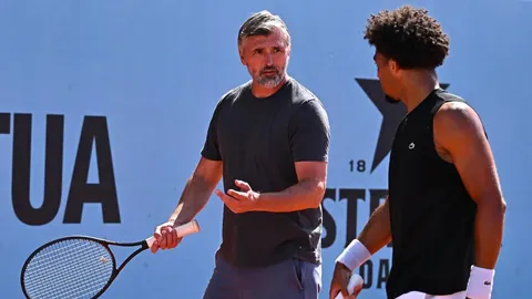 Goran Ivanišević s teniskim reketom razgovara s mladim igračem na terenu.