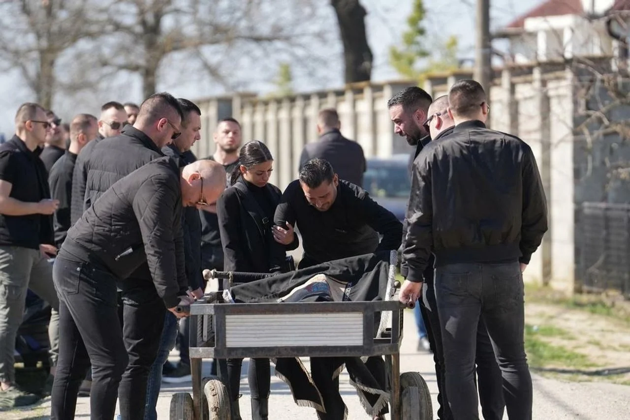 Muškarci okružuju i guraju pogrebna kolica s lijesom