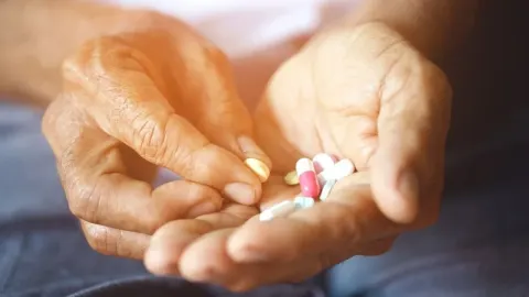 Starije ruke drže raznobojne tablete i kapsule