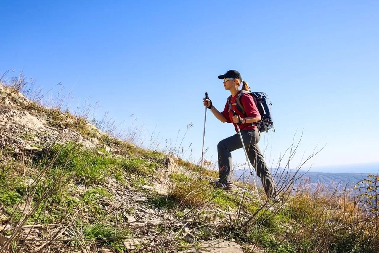 Žena planinari s ruksakom i štapovima uspinjući se na brdo