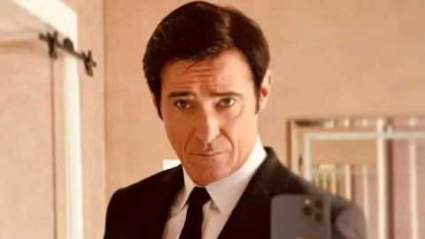 Goran Višnjić u tamnom odijelu s crnom kosom snima selfie u zrcalu.