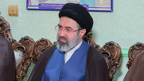 Mojtaba Hamenei s crnim turbanom i naočalama sjedi ispred karte