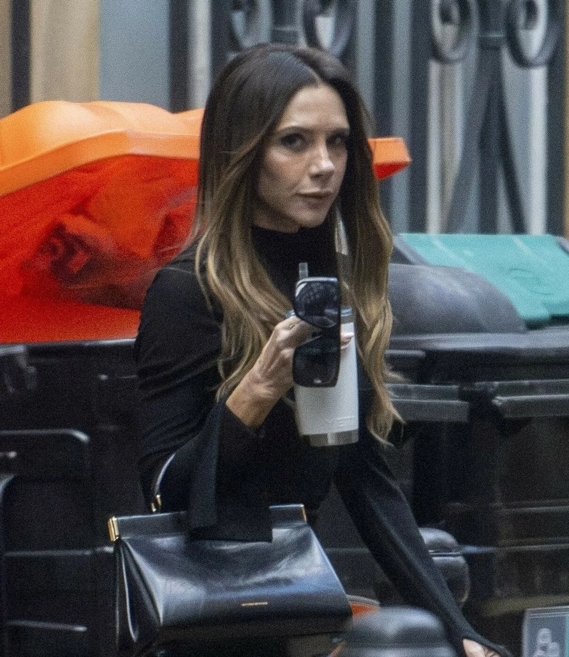 Victoria Beckham gleda prema kameri držeći torbu i čašu