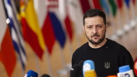 Volodimir Zelenski tijekom obraćanja novinarima ispred niza međunarodnih zastava.