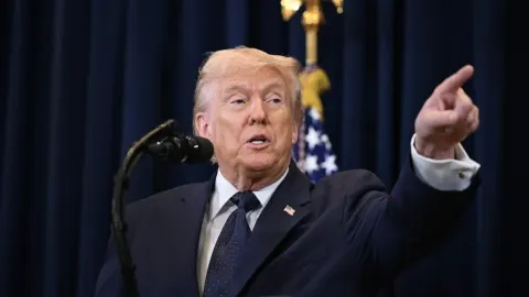 Donald Trump govori za govornicom i pokazuje prstom ispred američke zastave.