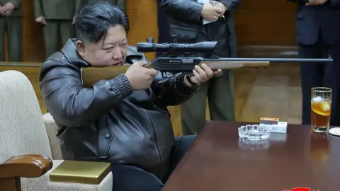Kim Jong-un cilja snajperskom puškom dok sjedi za stolom u kožnoj jakni.