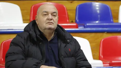 Trener Duško Vujošević sjedi na tribinama u crnoj sportskoj jakni.