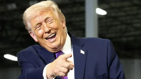 Donald Trump se smije i pokazuje prstom prema kameri u tamnom odijelu.