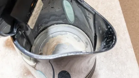 Unutrašnjost električnog kuhala za vodu s vidljivim naslagama kamenca na dnu.