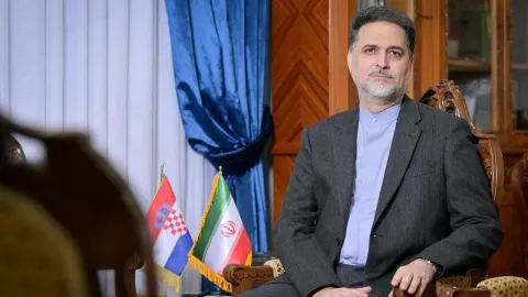 Muškarac u sivom odijelu sjedi pored iranske i hrvatske zastavice