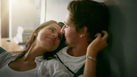 Mladi par u intimnom trenutku gleda se u oči u spavaćoj sobi.