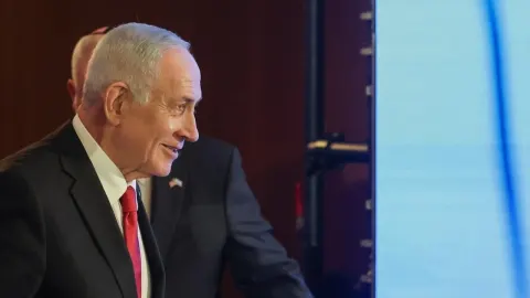 Benjamin Netanyahu u crnom odijelu s crvenom kravatom gleda u stranu i smiješi se.