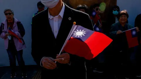 Muškarac u odijelu drži zastavu Tajvana dok ljudi u pozadini promatraju