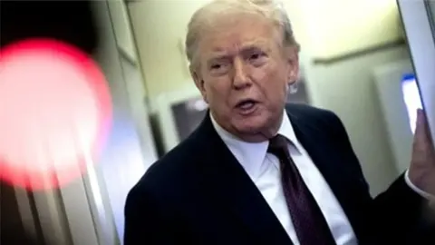 Donald Trump u odijelu s kravatom razgovara u unutrašnjosti zrakoplova Air Force One.