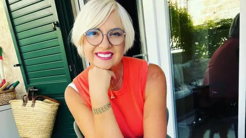 Nasmijana Danijela Dvornik s plavom kosom i naočalama u narančastoj majici.