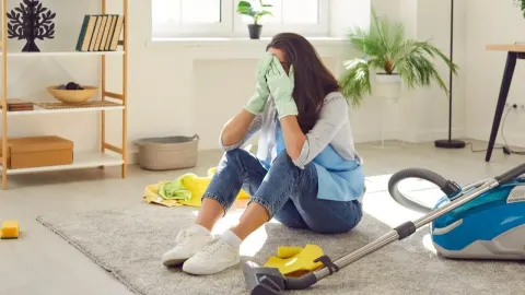 Razočarana žena sjedi na podu pored usisavača i sredstava za čišćenje.