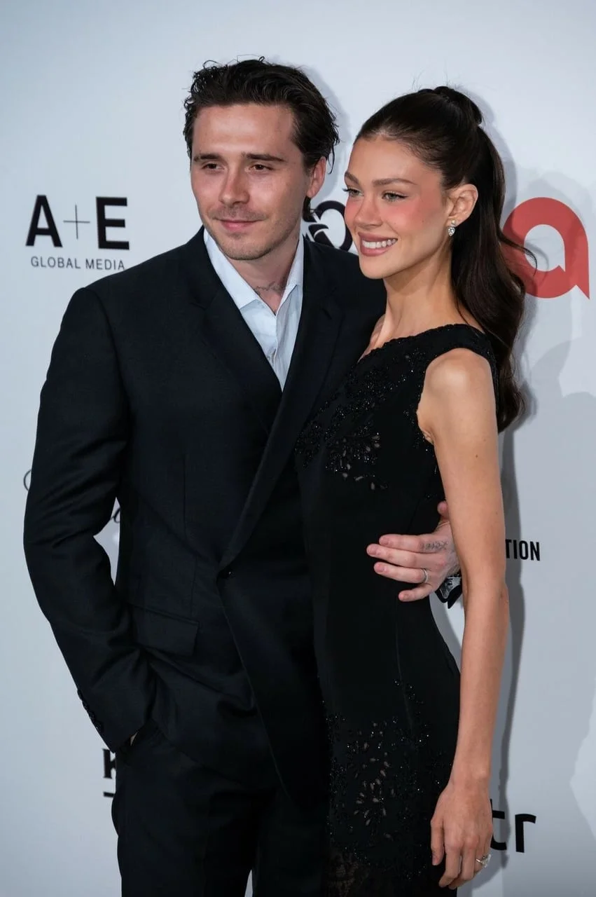 Brooklyn Beckham u crnom odijelu i Nicola Peltz ispred brendiranog zida zaklade Eltona Johna.