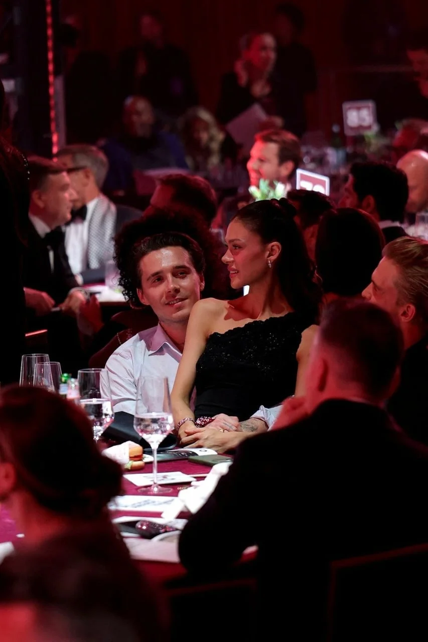 Široki kadar Brooklyna Beckhama i Nicole Peltz za stolom okruženih uzvanicima.