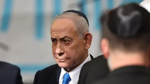 Benjamin Netanyahu u krupnom planu s ozbiljnim izrazom lica tijekom javnog događaja.