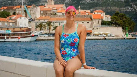 Dina Levačić u kupaćem kostimu s kapicom i naočalama sjedi uz more.